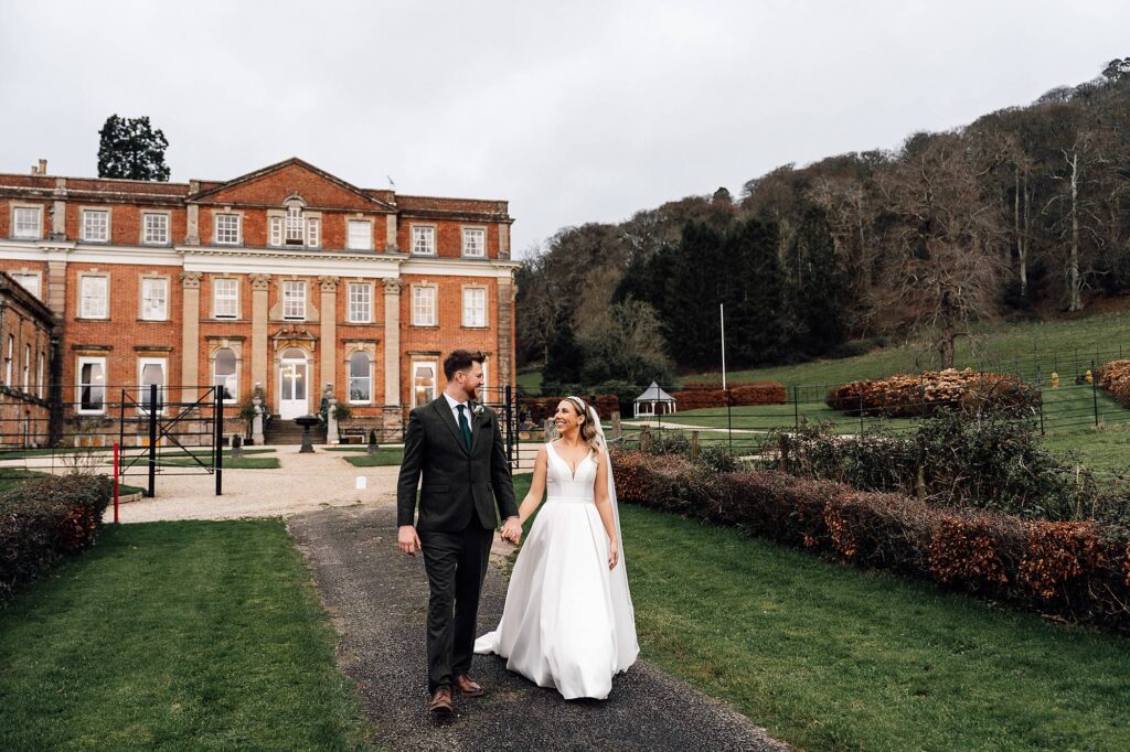 Bride & groom walk hand in hand outside Crowcombe Court