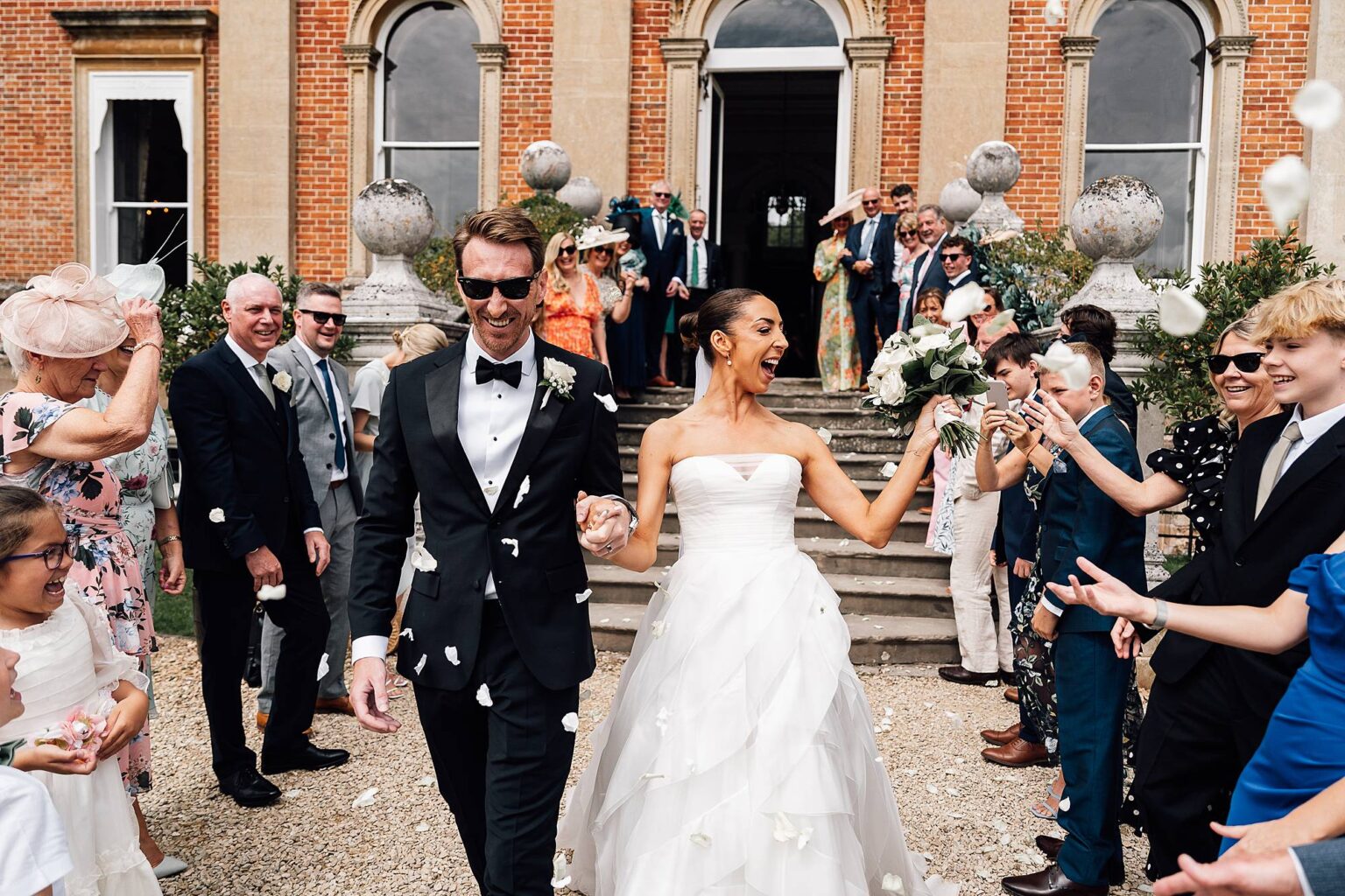 Beautiful bride & groom walk down a confetti tunnel outside Crowcombe Court.